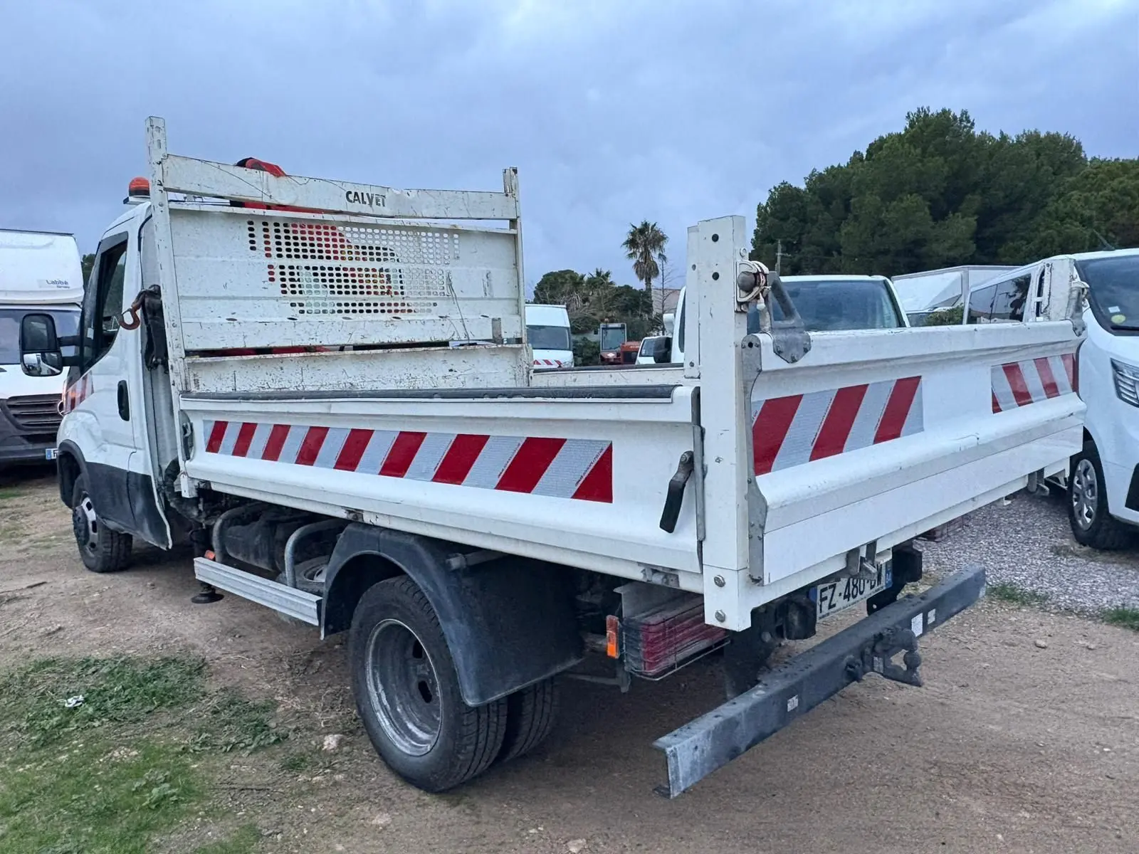 IVECO Daily Chassis Cabine blanc vu en 3/4 arrière droit avec benne basculante et marquages rouges réfléchissants.
