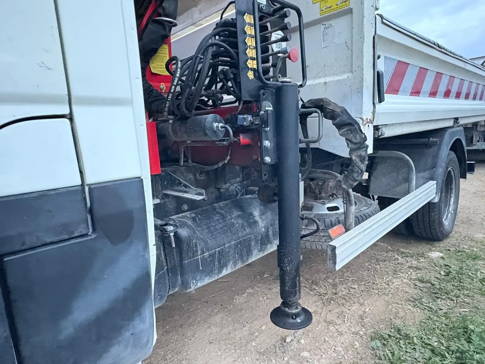 Détail côté gauche d’une benne blanche Iveco Daily 35C14 avec grue Palfinger et stabilisateur déployé.