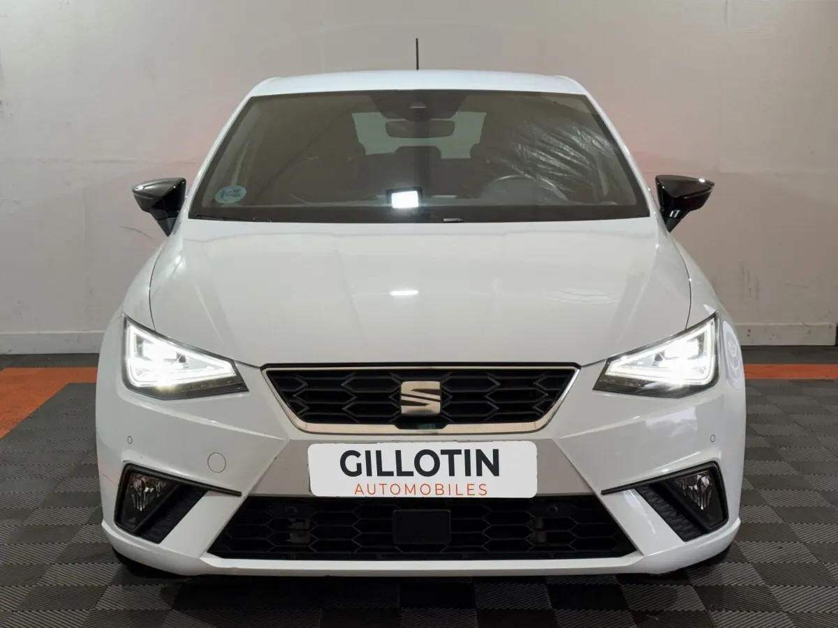 Vue avant d'une SEAT Ibiza 1.0 TSI 110 FR blanche avec phares LED allumés et calandre noire hexagonale.