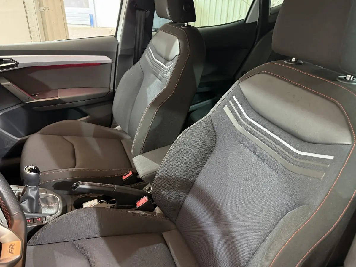 Vue intérieure côté conducteur de la SEAT Ibiza 1.0 TSI 110 FR 2024, sièges noirs avec surpiqûres rouges et levier de vitesses manuel.