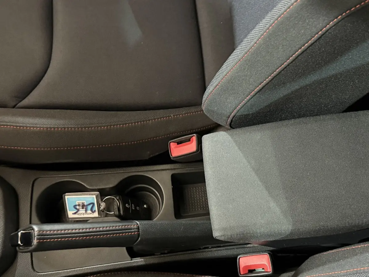 Gros plan intérieur sur la console centrale de la SEAT Ibiza blanche, frein à main cuir avec surpiqûres rouges et porte-gobelets.