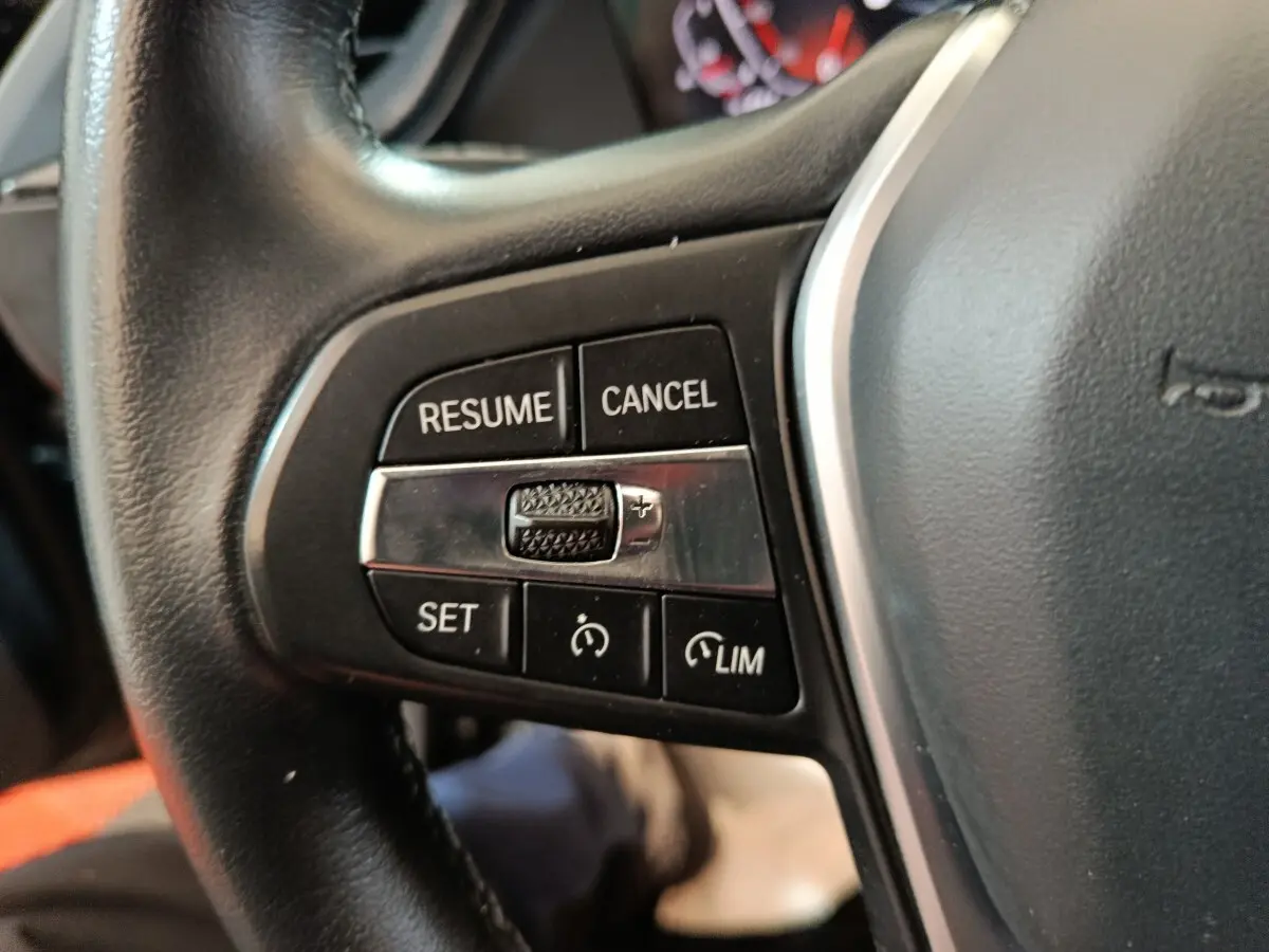 Gros plan sur les commandes de régulateur de vitesse au volant cuir noir de la BMW Série 1 118i Edition Sport 2023.