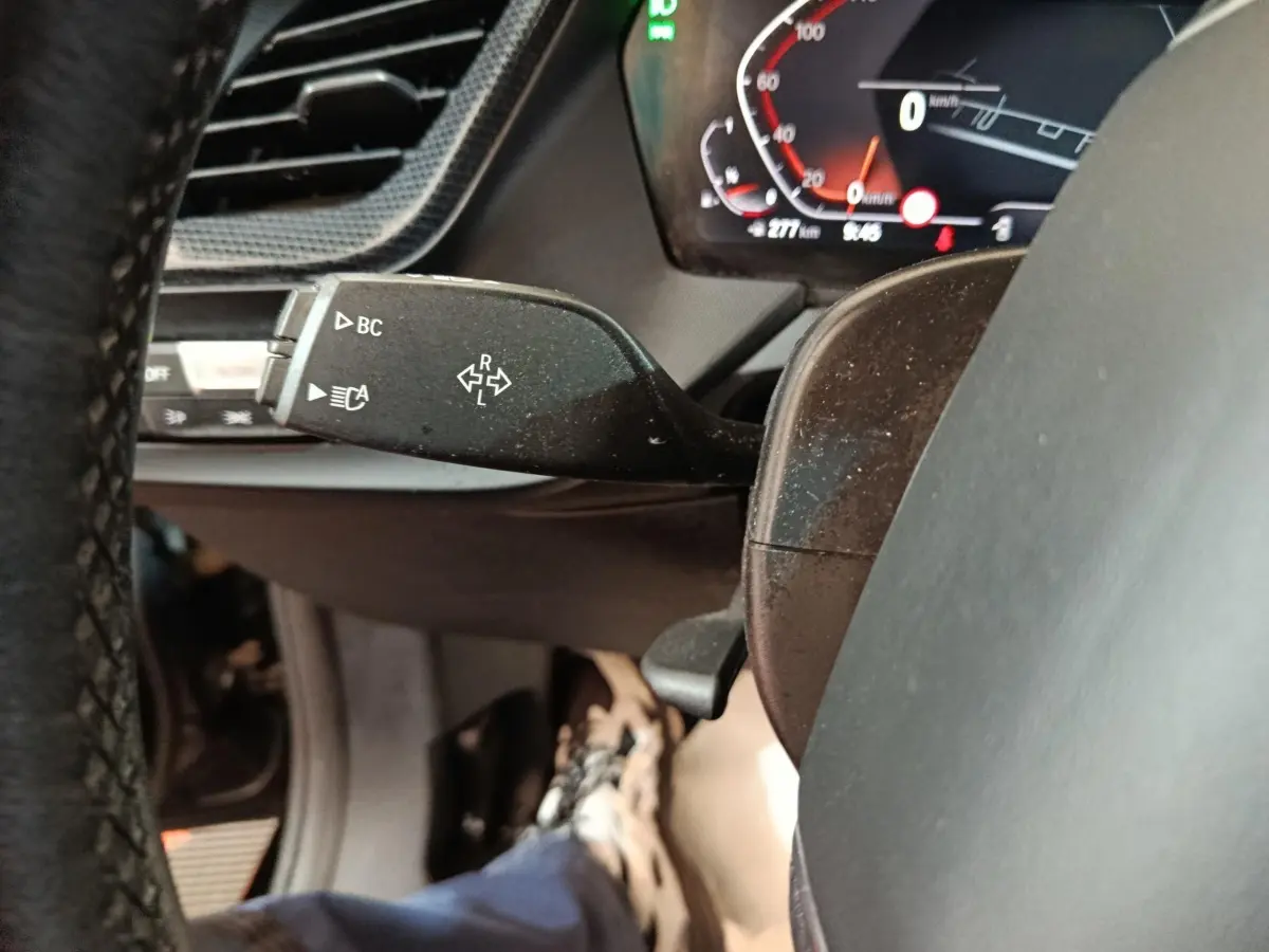 Gros plan sur la manette de clignotant gauche et le tableau de bord numérique d'une BMW Série 1 118i noire de 2023.