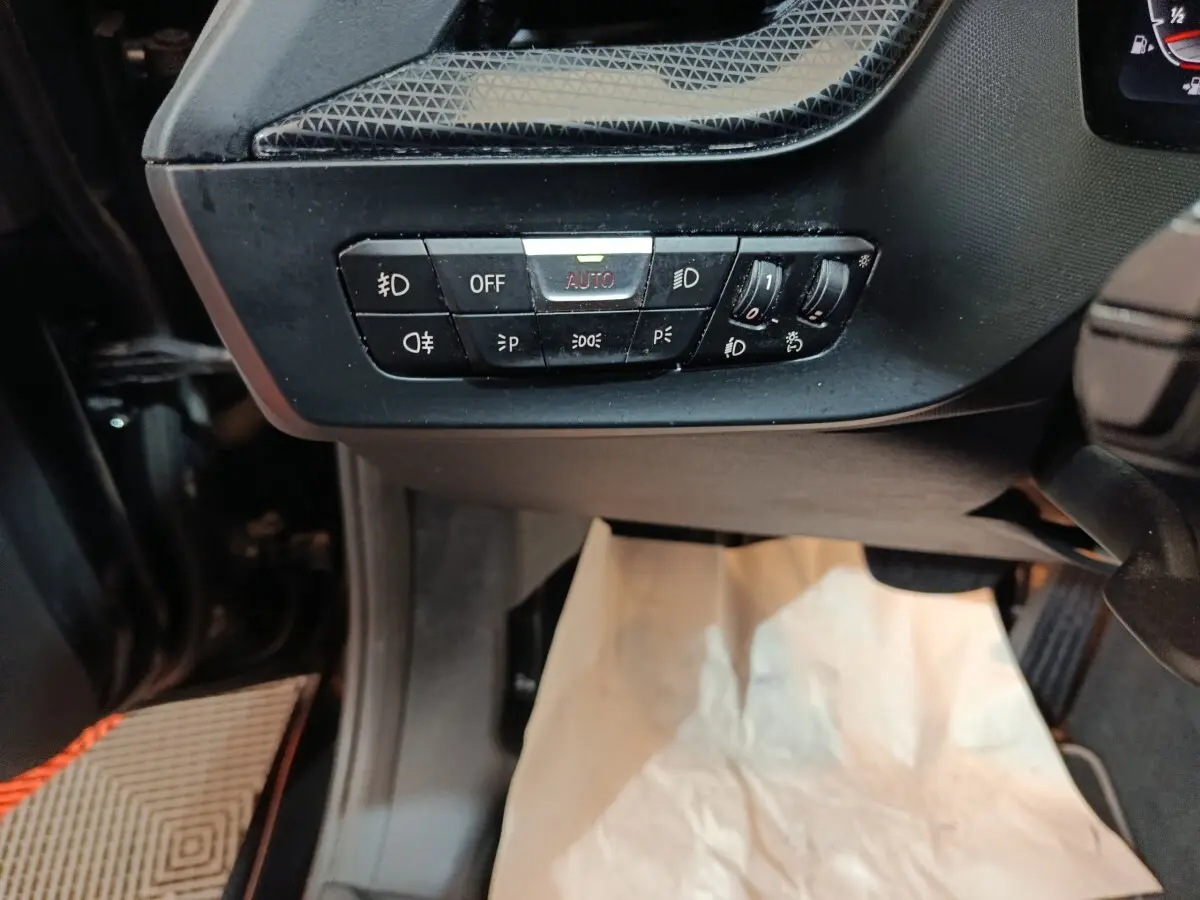 Vue rapprochée du tableau de bord côté gauche d’une BMW Série 1 noire, avec commandes d’éclairage et réglages lumineux.