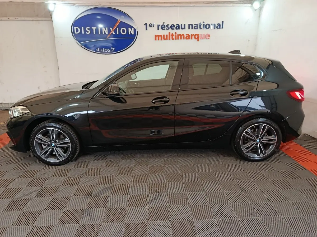 BMW Série 1 118i Edition Sport noire vue de profil côté gauche, avec jantes alliage et feux arrière LED allumés.