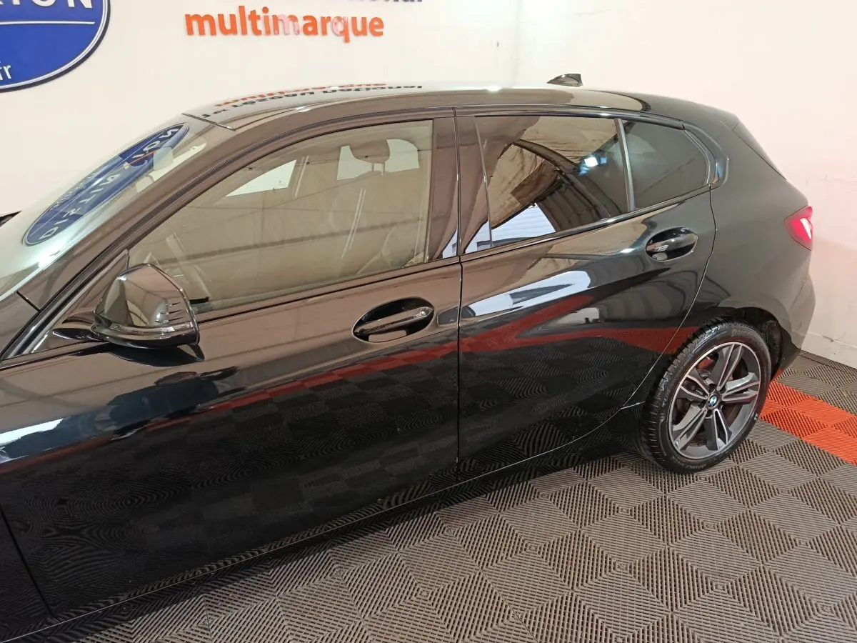 Vue latérale côté gauche d'une BMW Série 1 118i Edition Sport noire avec jantes alliage et rétroviseurs ton caisse.