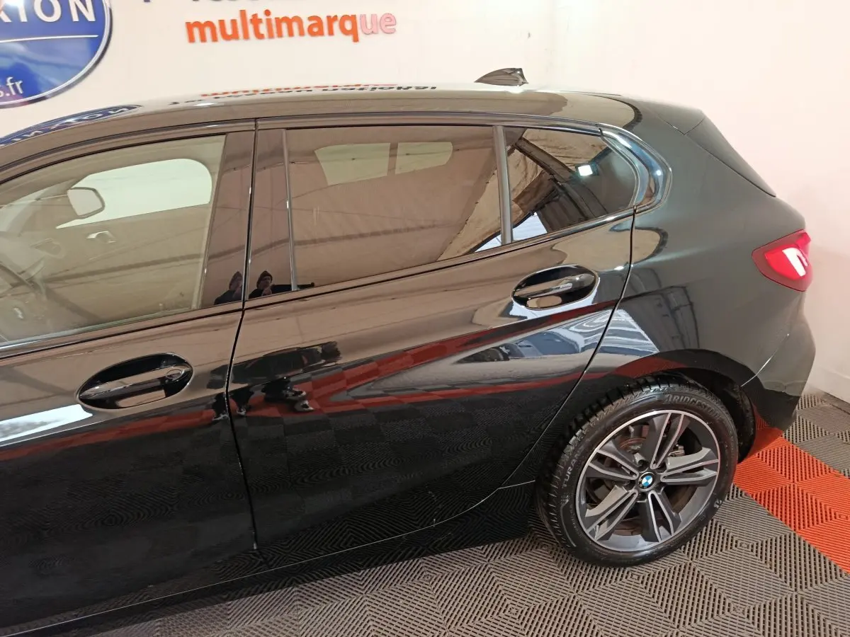 Vue latérale côté gauche d'une BMW Série 1 noire, mettant en valeur la porte arrière et la roue arrière alliage.