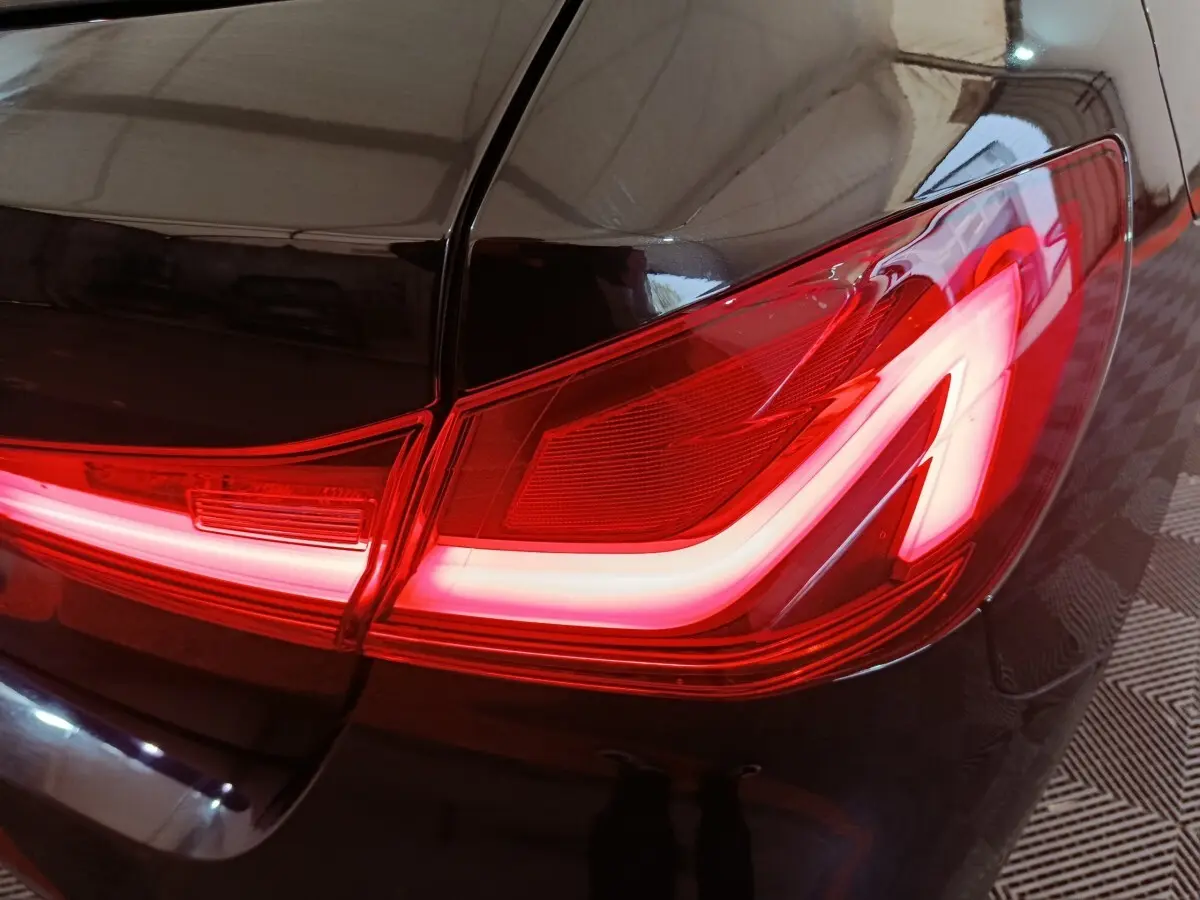 Gros plan sur le feu arrière droit allumé d’une BMW Série 1 118i Edition Sport noire, finition brillante.