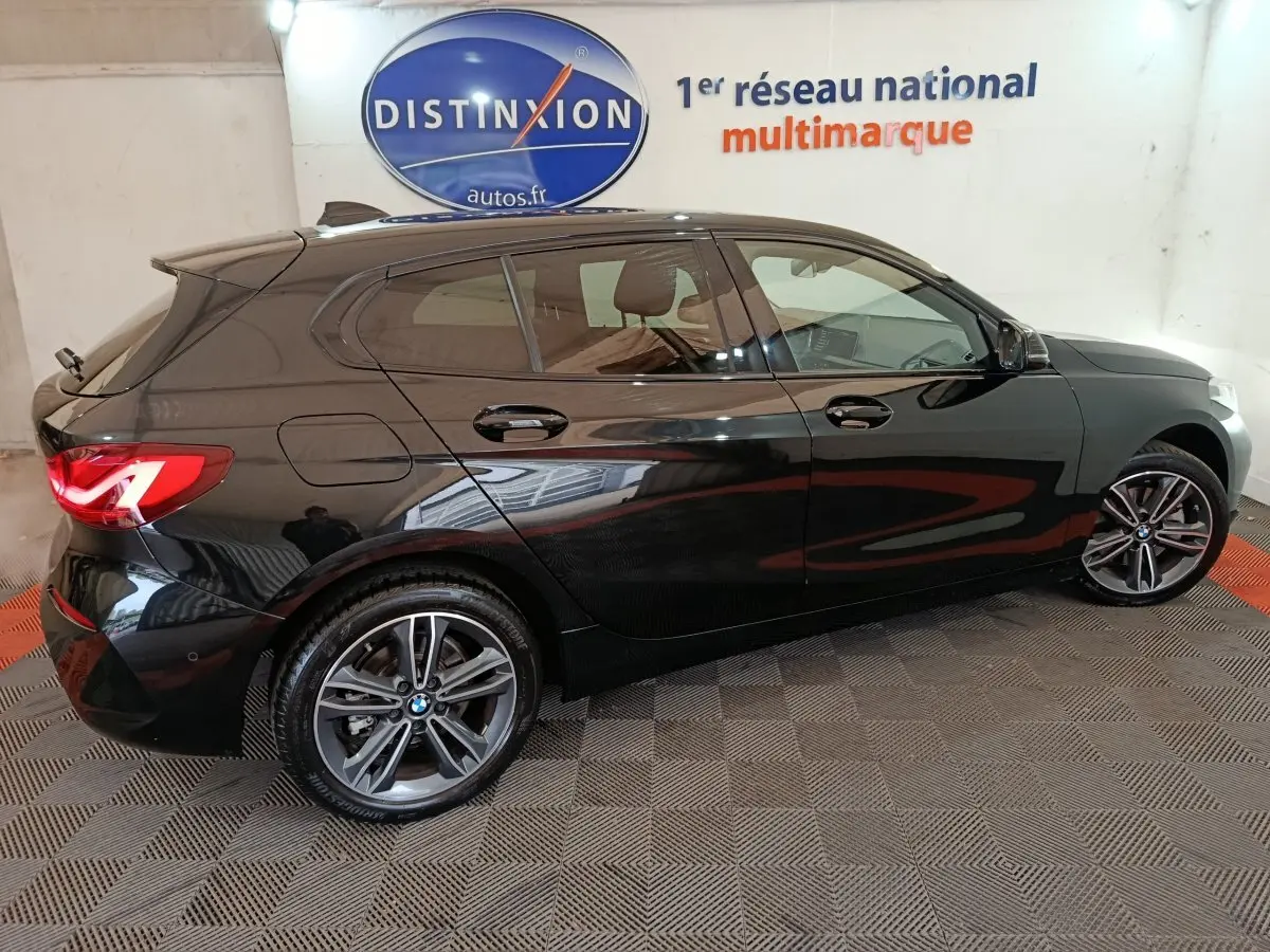 BMW Série 1 118i Edition Sport noire vue de profil côté gauche, avec jantes alliage et feux arrière LED allumés.