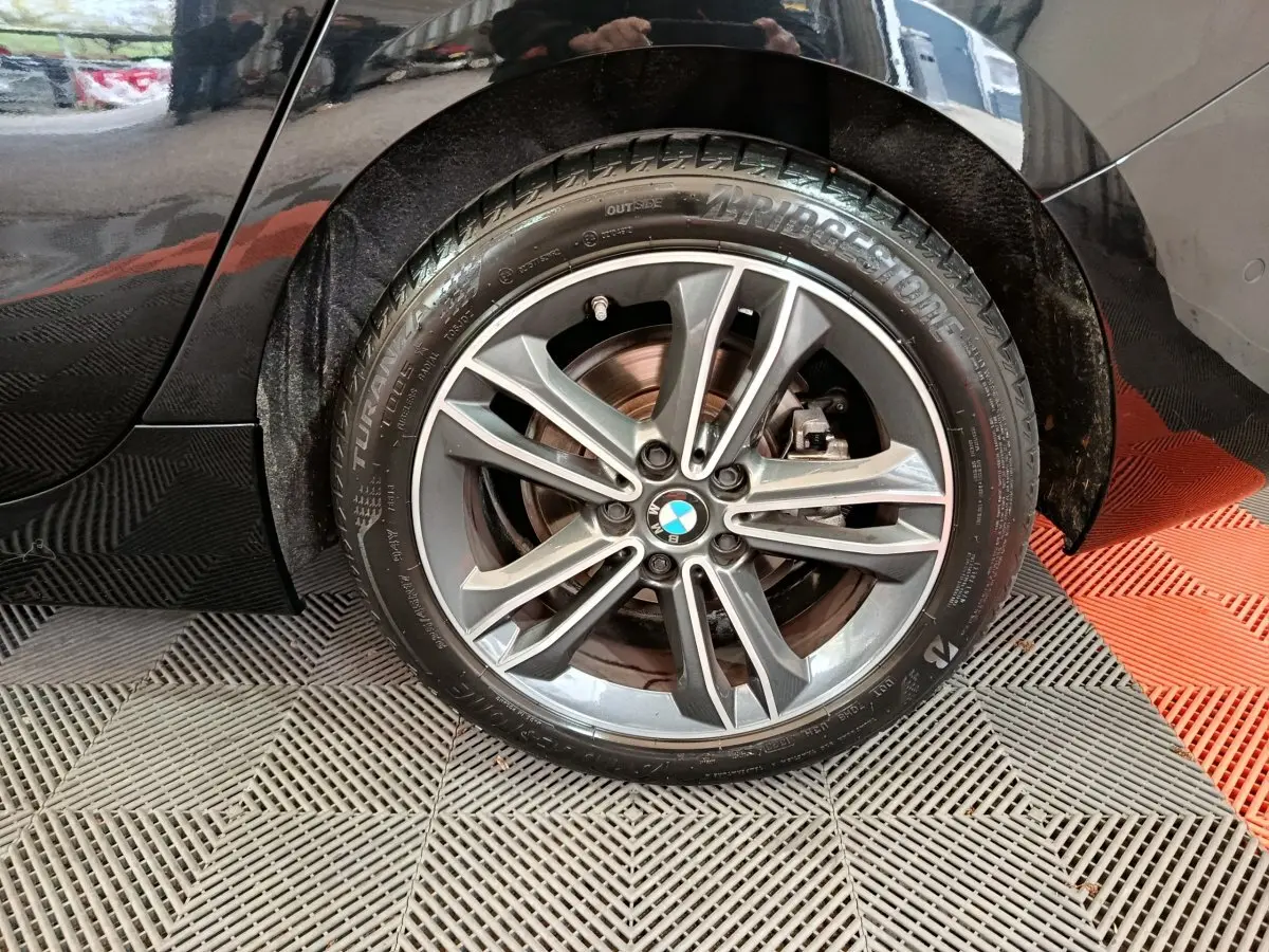 Gros plan sur la roue arrière droite noire d'une BMW Série 1 118i Edition Sport avec jante alliage et logo BMW visible.