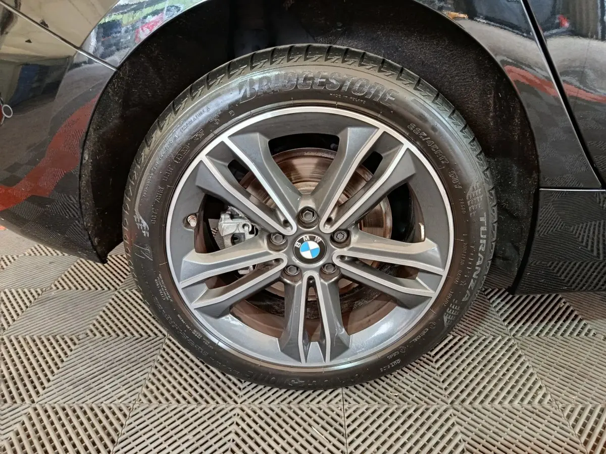 Gros plan sur la roue avant gauche noire d'une BMW Série 1 118i Edition Sport avec jante alliage gris foncé.
