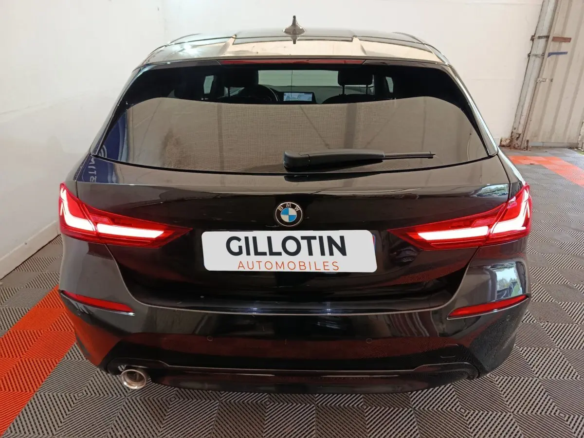 Vue arrière d’une BMW Série 1 118i Edition Sport noire avec feux LED allumés dans un garage.