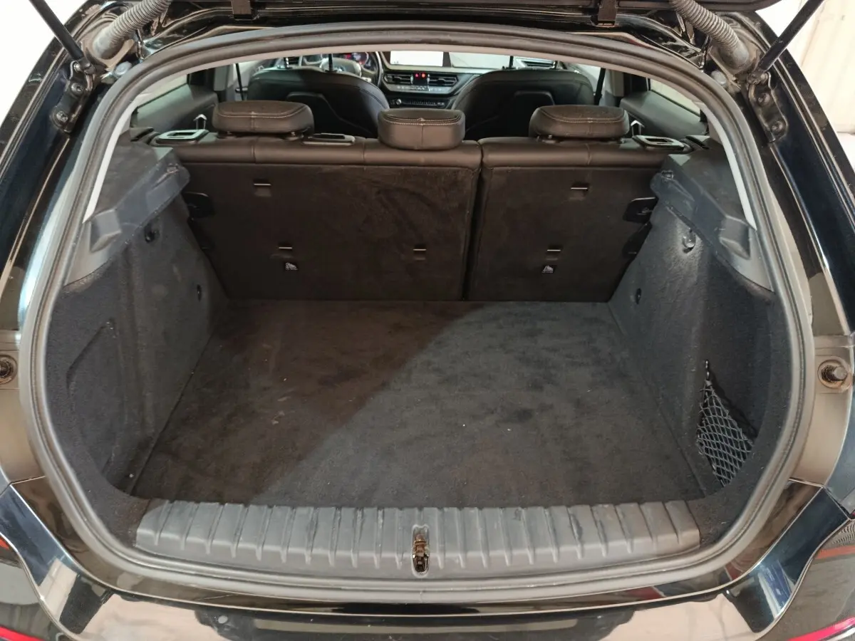 Coffre ouvert vu de l'arrière d'une BMW Série 1 118i Edition Sport noire, montrant l'espace de chargement et la banquette arrière.