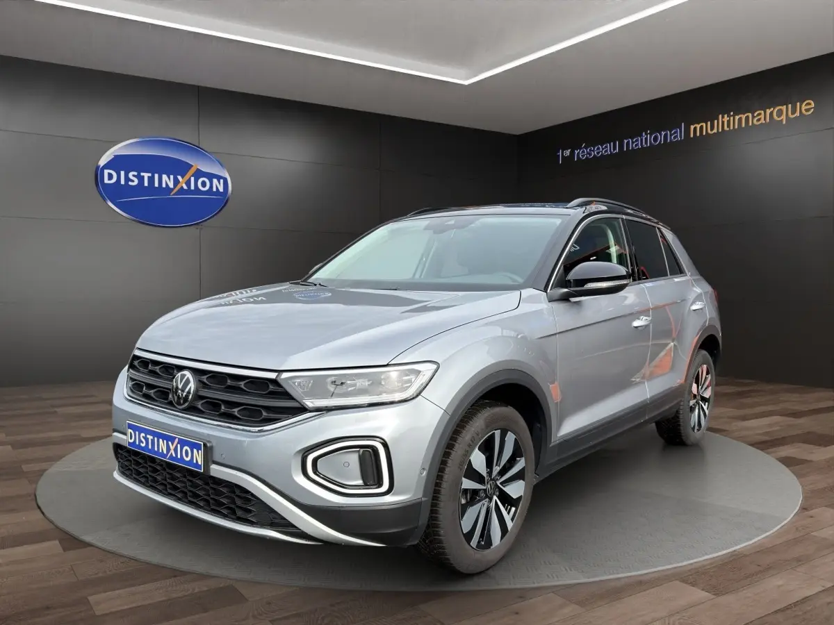 Volkswagen T-Roc gris clair en 3/4 avant droit, avec jantes alliage et calandre noire distinctive.