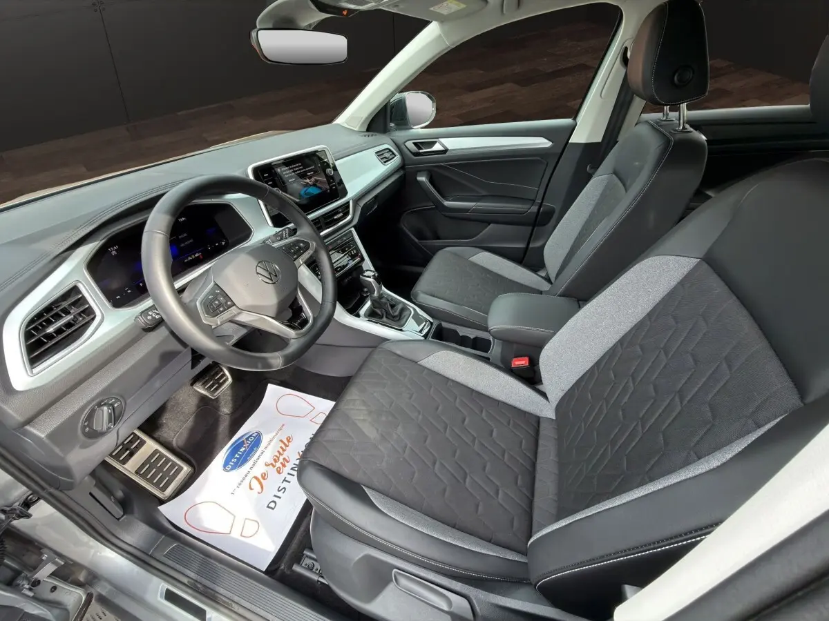Vue intérieure côté conducteur du Volkswagen T-Roc 2.0 TDI gris clair, montrant sièges bi-matière et tableau de bord moderne.