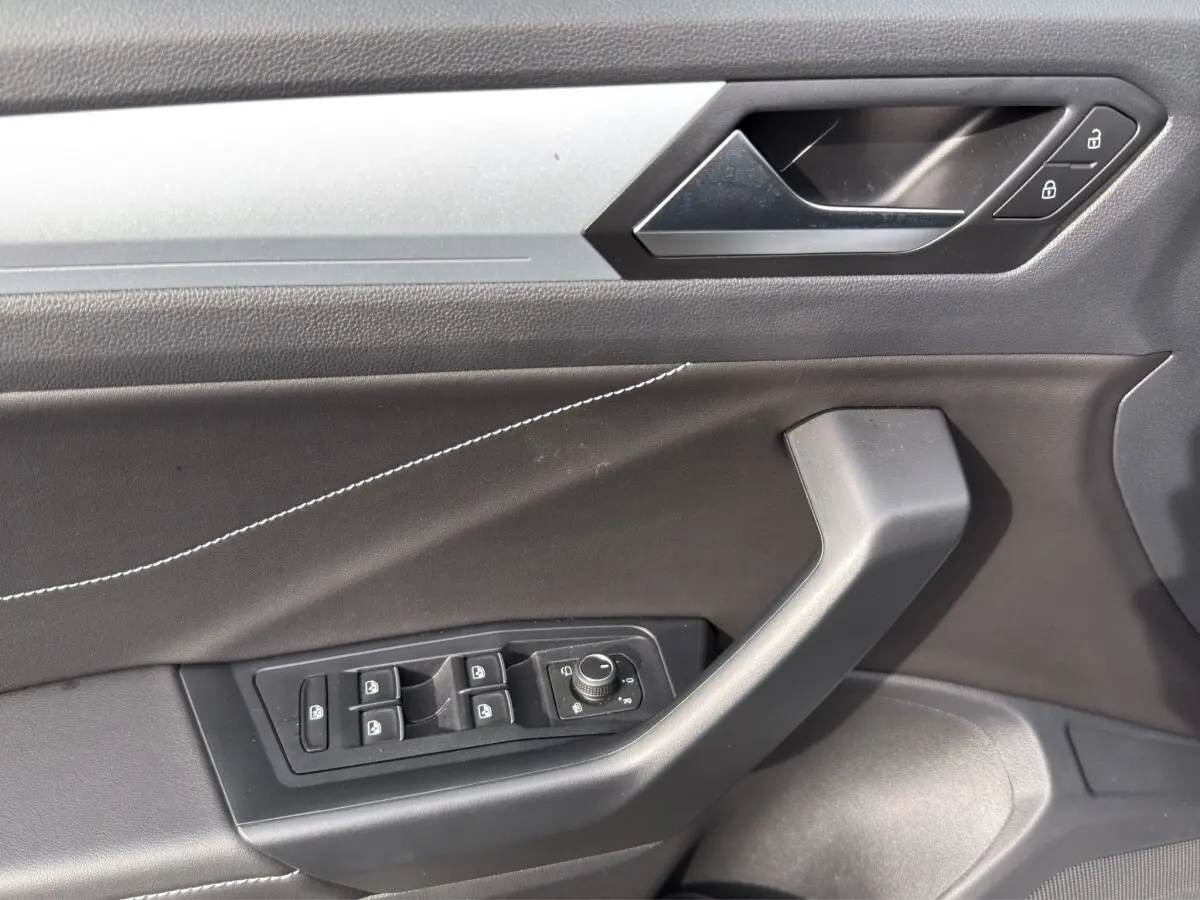 Gros plan sur la porte côté conducteur du Volkswagen T-Roc gris clair, montrant les commandes des vitres et la poignée intérieure.