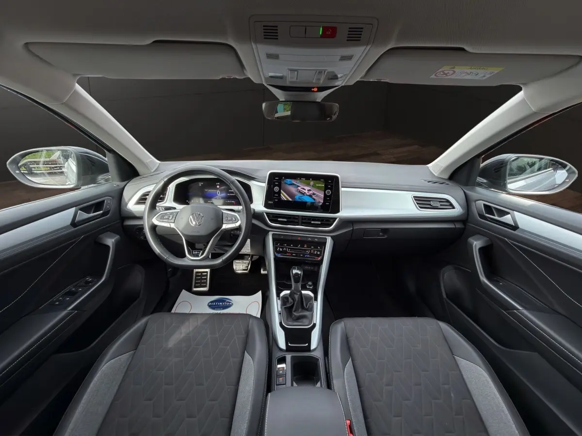 Vue intérieure avant du Volkswagen T-Roc gris clair 2025, avec tableau de bord numérique et écran tactile central.