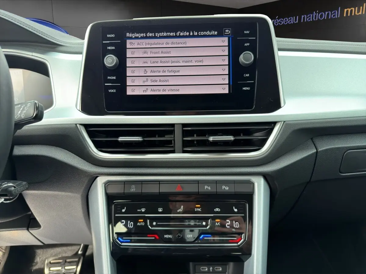 Vue intérieure du tableau de bord du Volkswagen T-Roc 2025, écran tactile central affichant les réglages d'aide à la conduite.