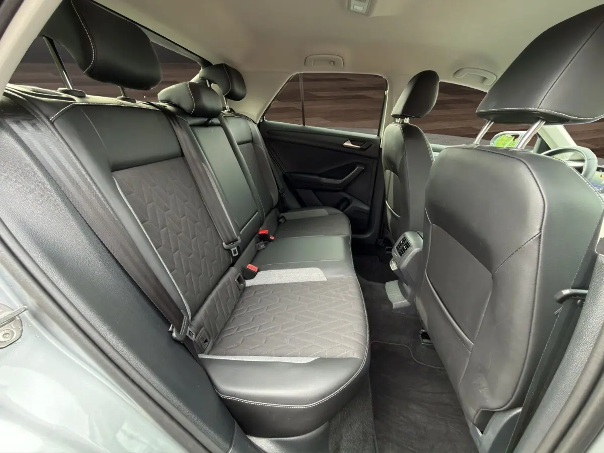 Vue intérieure arrière du Volkswagen T-Roc 2025 gris clair, montrant la banquette 3 places en tissu et cuir avec ceintures de sécurité.