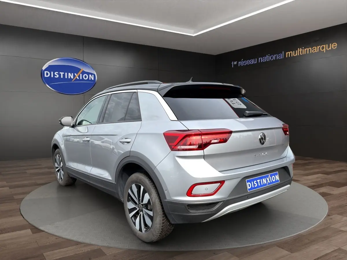 Vue 3/4 arrière d'un Volkswagen T-Roc gris clair avec attelage amovible dans un showroom.