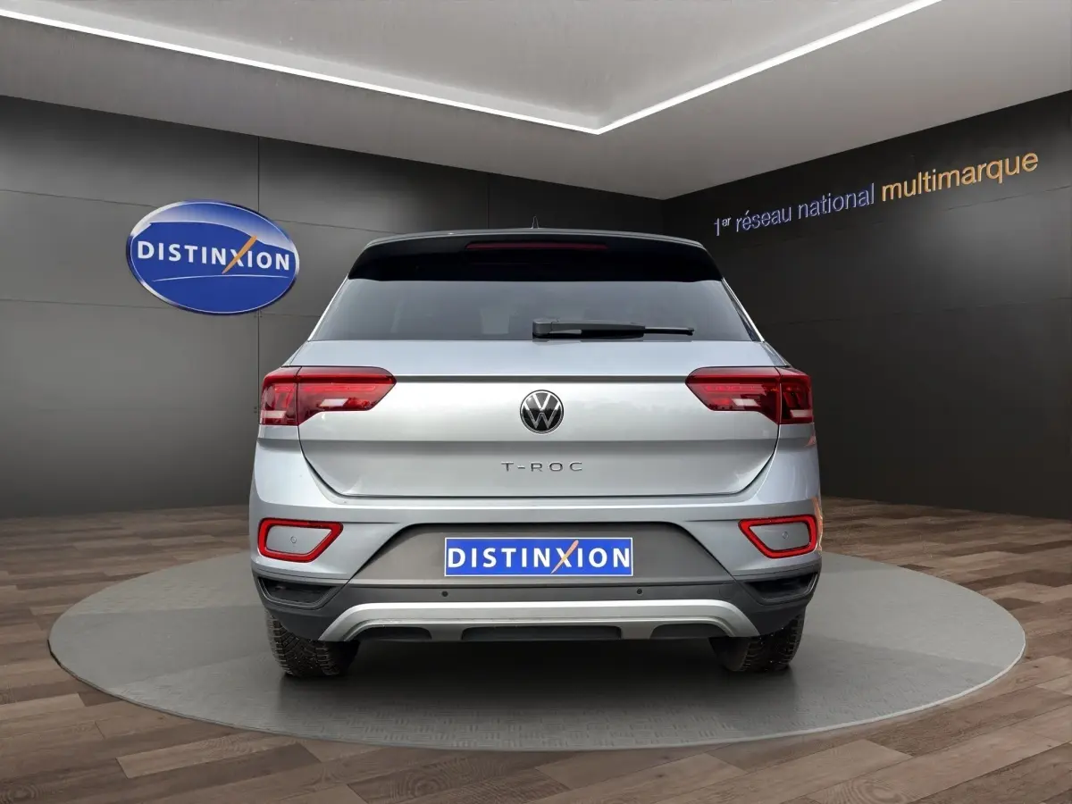 Vue arrière d'un Volkswagen T-Roc gris clair 2025 avec feux LED et attelage amovible visible en showroom.