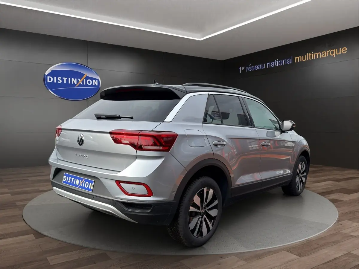 Vue 3/4 arrière droite d'un Volkswagen T-Roc gris clair avec jantes noires et grises, dans un showroom.
