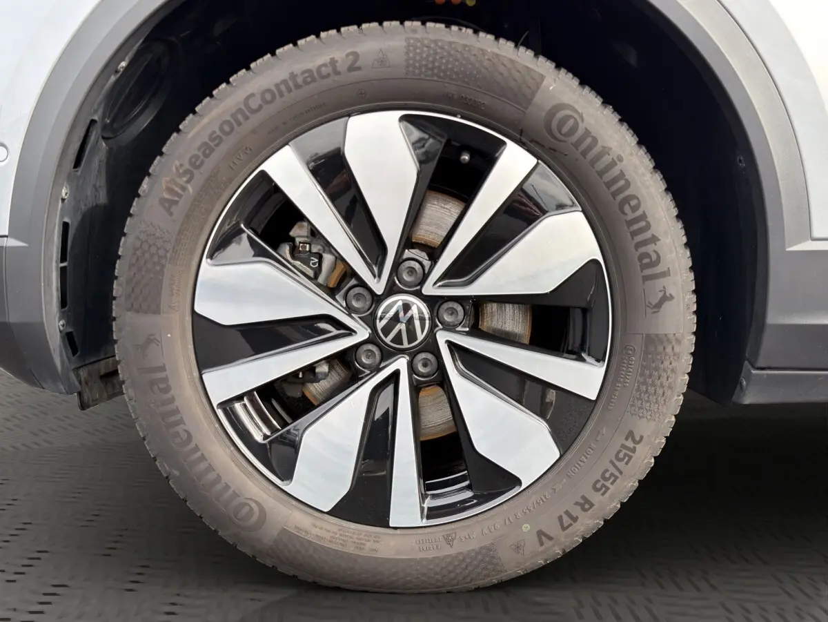 Gros plan sur la roue avant droite du Volkswagen T-Roc gris clair, jante alliage bicolore avec logo VW central.