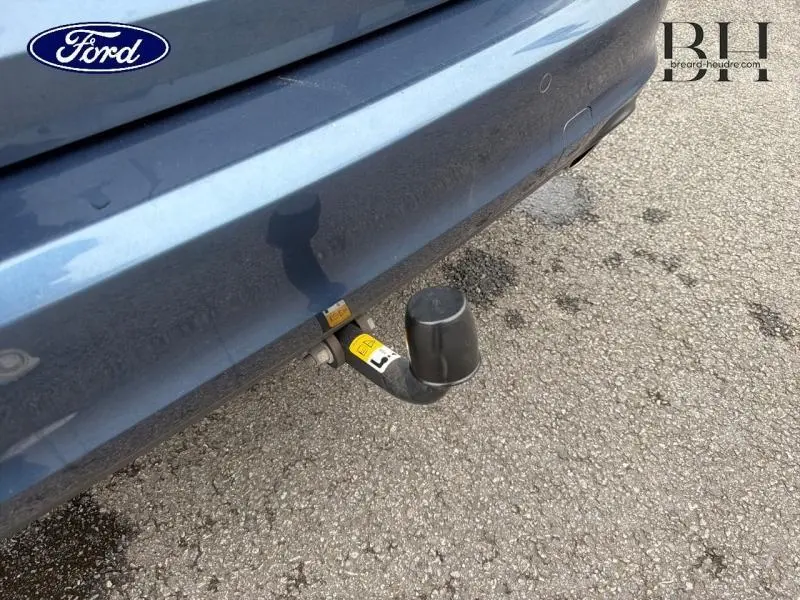 Gros plan sur l'attelage arrière d'une Ford Focus SW bleu azur métallisé, avec pare-chocs et sol asphalté visibles.