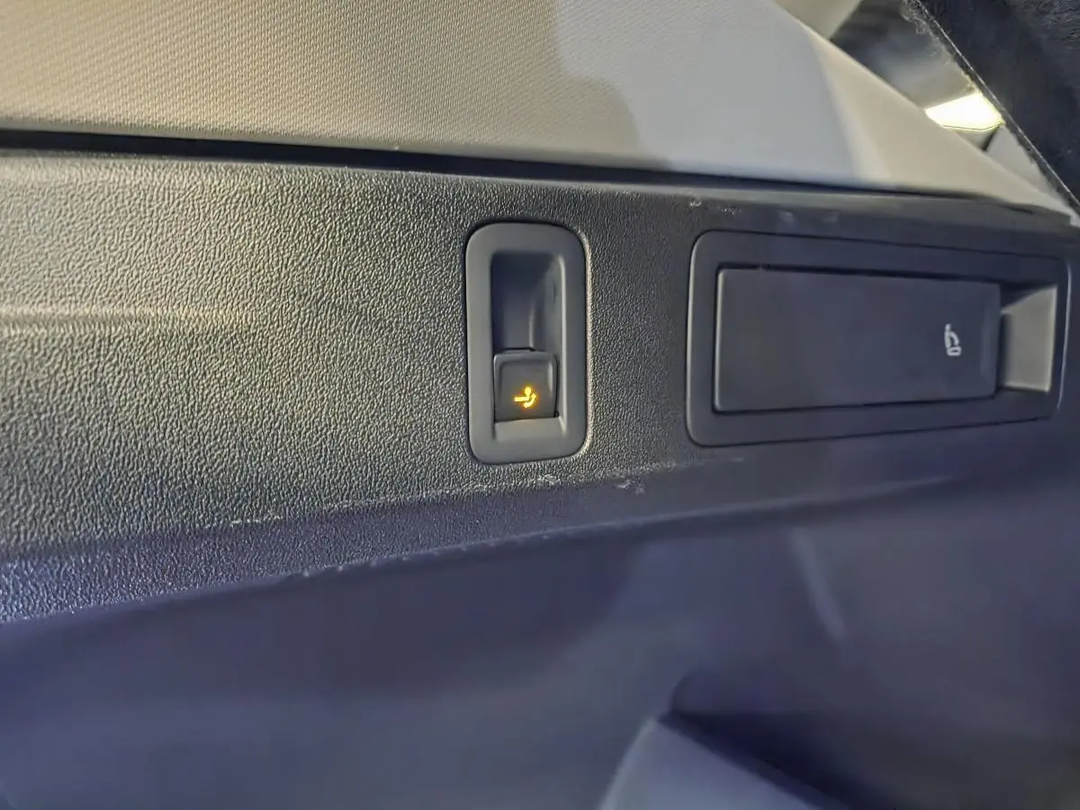 Gros plan sur le bouton de rabattement électrique des sièges arrière dans le coffre du Volkswagen Tiguan noir.