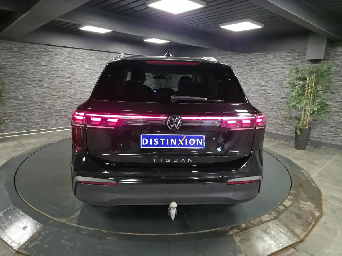 Vue arrière d'un Volkswagen Tiguan noir 2025 avec feux LED allumés et crochet d'attelage escamotable visible.