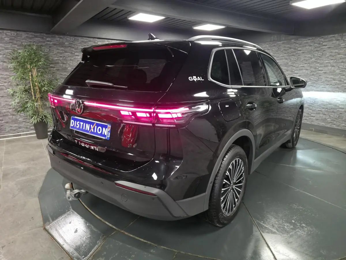 Volkswagen Tiguan noir en 3/4 arrière droit avec feux LED allumés et crochet d'attelage escamotable visible.