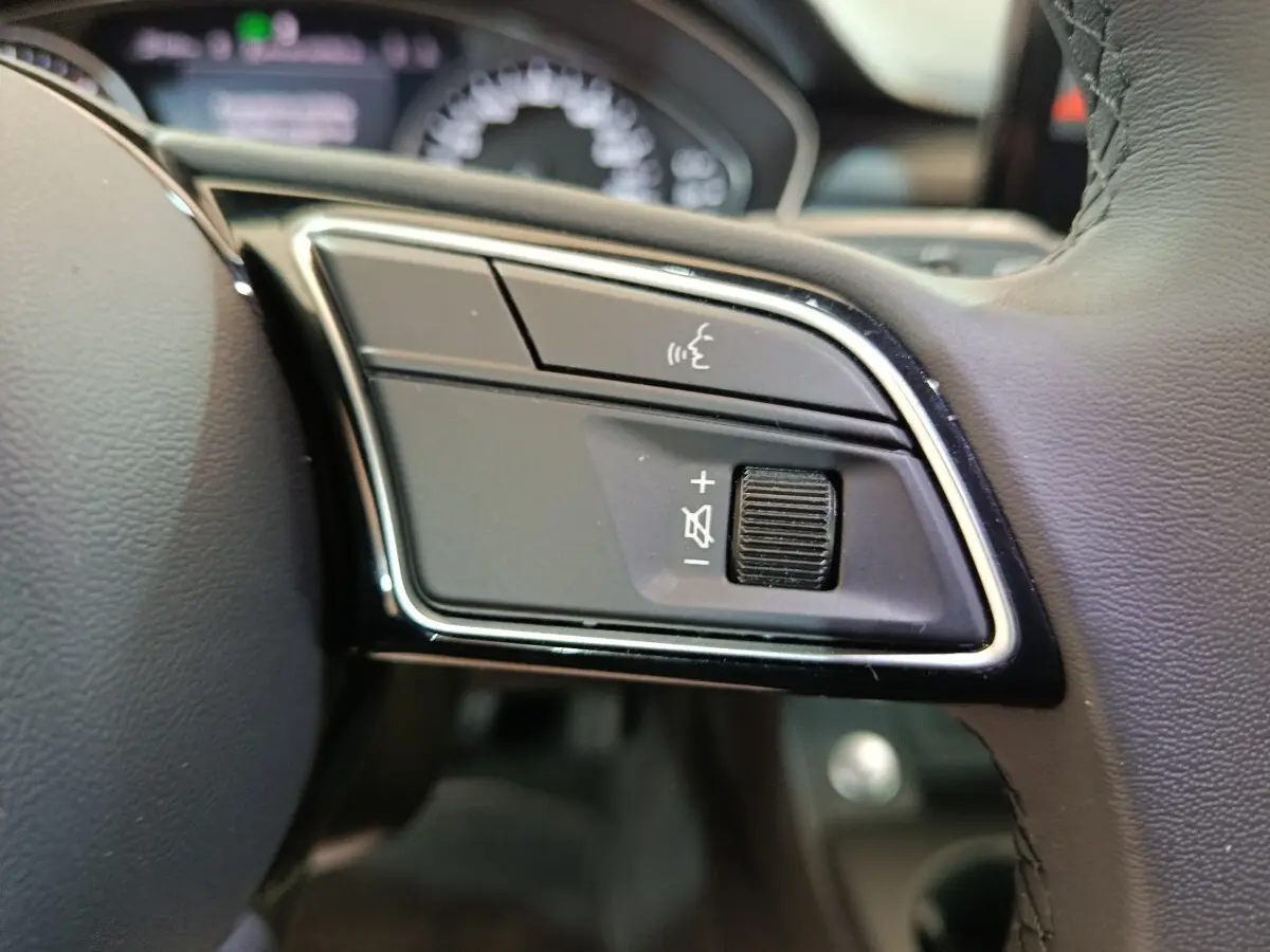 Gros plan sur les commandes vocales et volume au volant cuir noir de l'Audi A4 35 TFSI Business Line 2024.