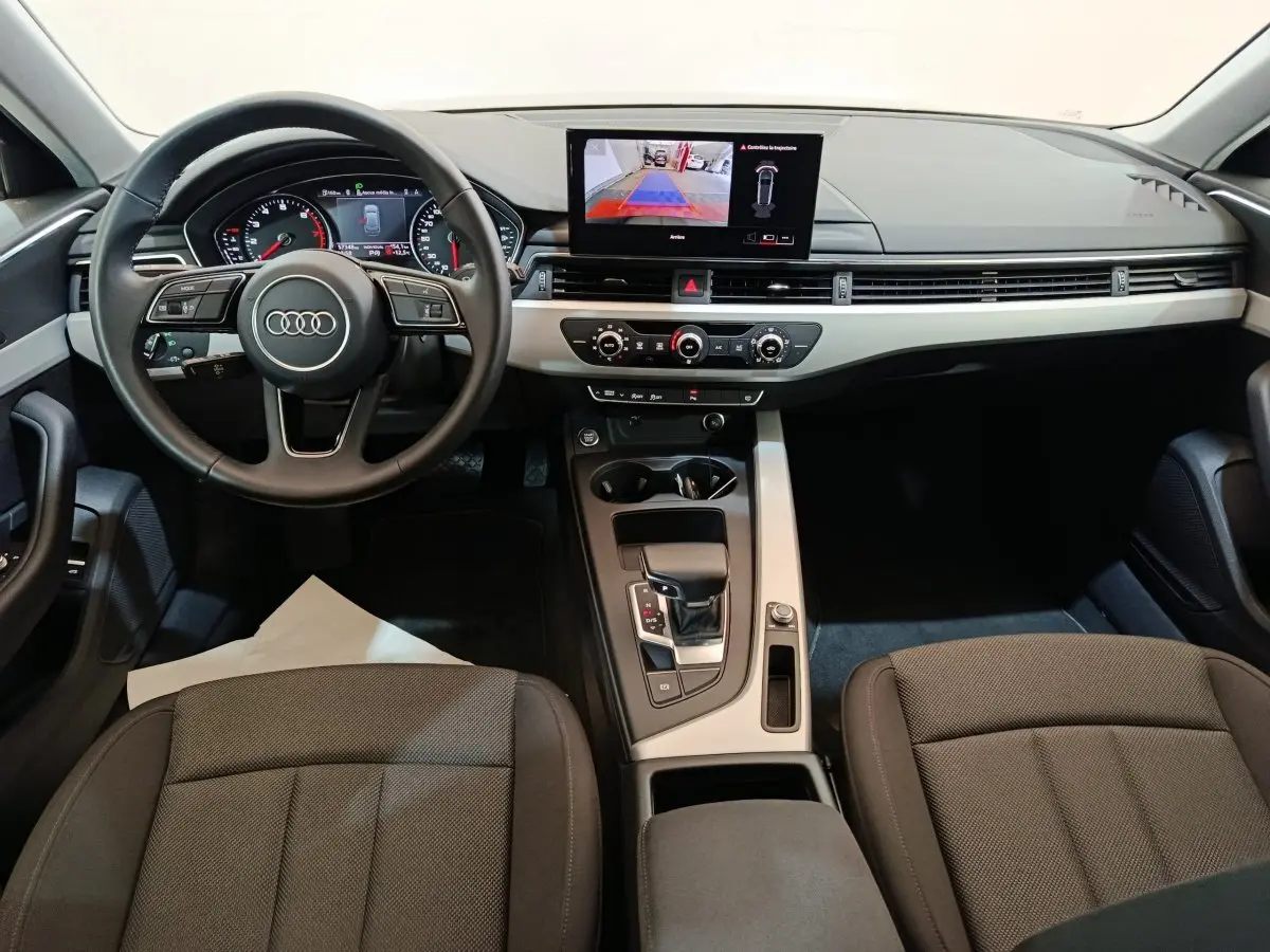 Vue intérieure avant de l'Audi A4 35 TFSI Business Line 2024, tableau de bord noir avec écran central tactile et volant cuir multifonctions.