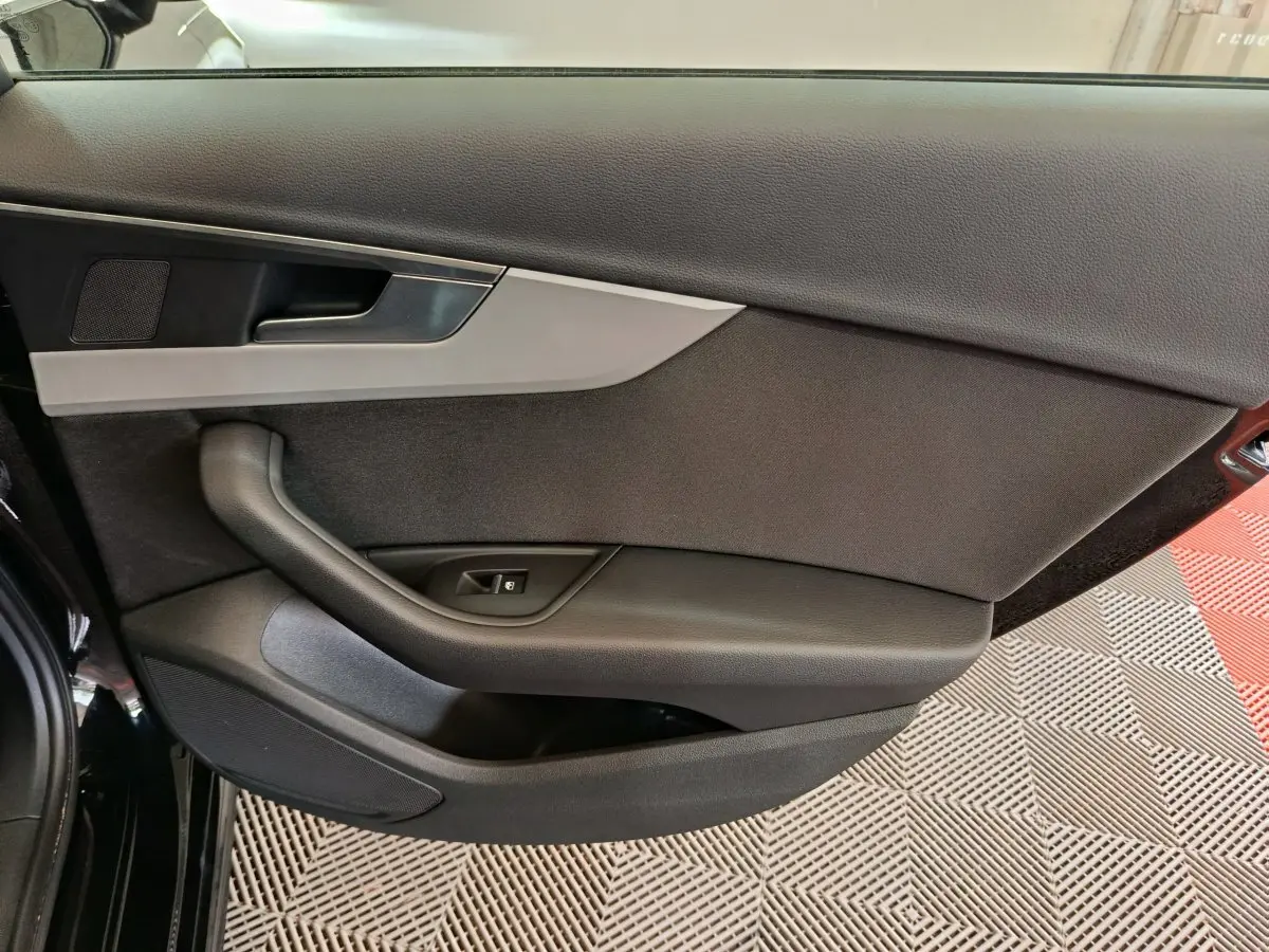 Vue rapprochée de la porte avant gauche noire de l'Audi A4 35 TFSI 2024 avec poignée et commande de vitre.