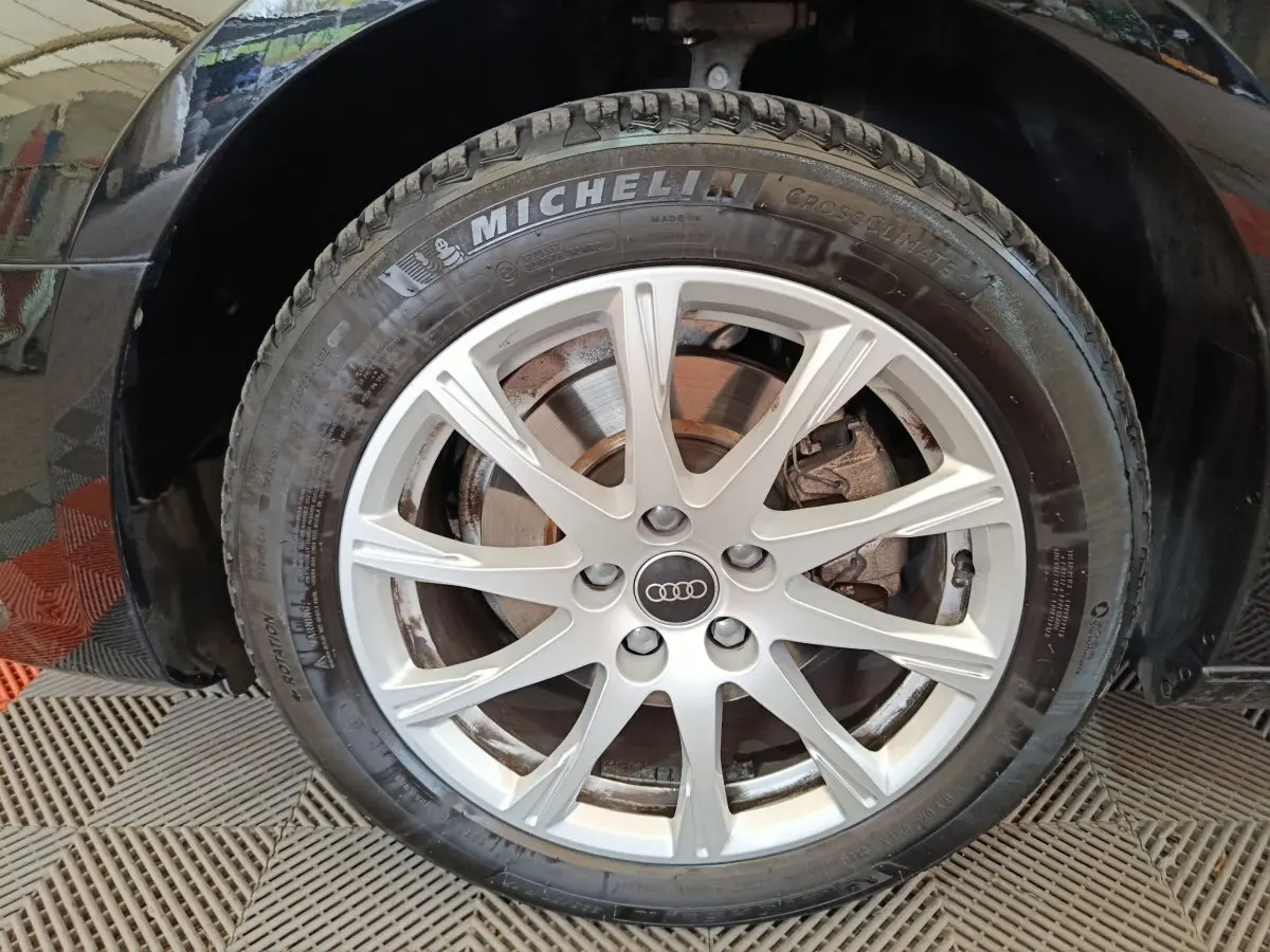 Gros plan sur la roue avant droite d'une Audi A4 noire 2024 avec jante argentée et pneu Michelin CrossClimate.
