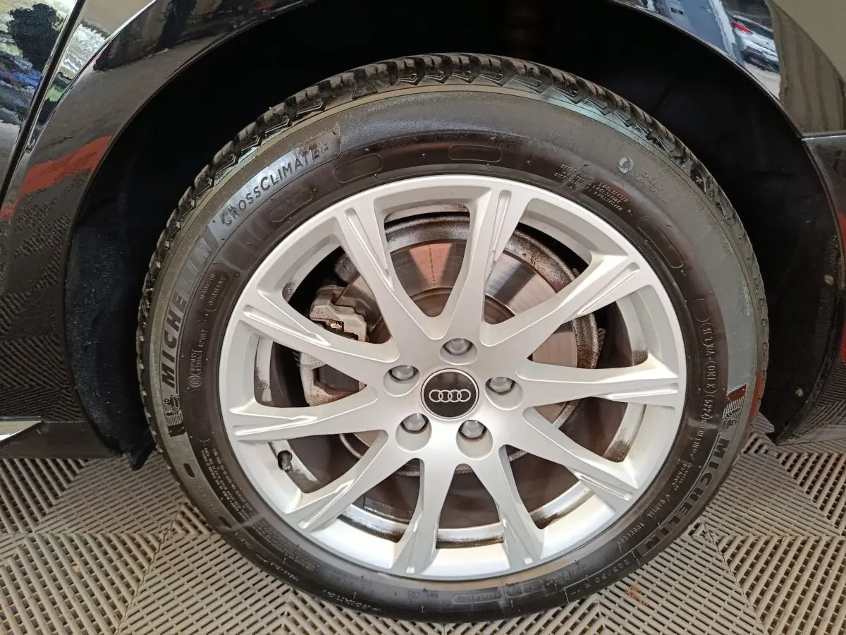 Gros plan sur la roue avant droite d'une Audi A4 noire, jante alliage argentée avec logo Audi central.