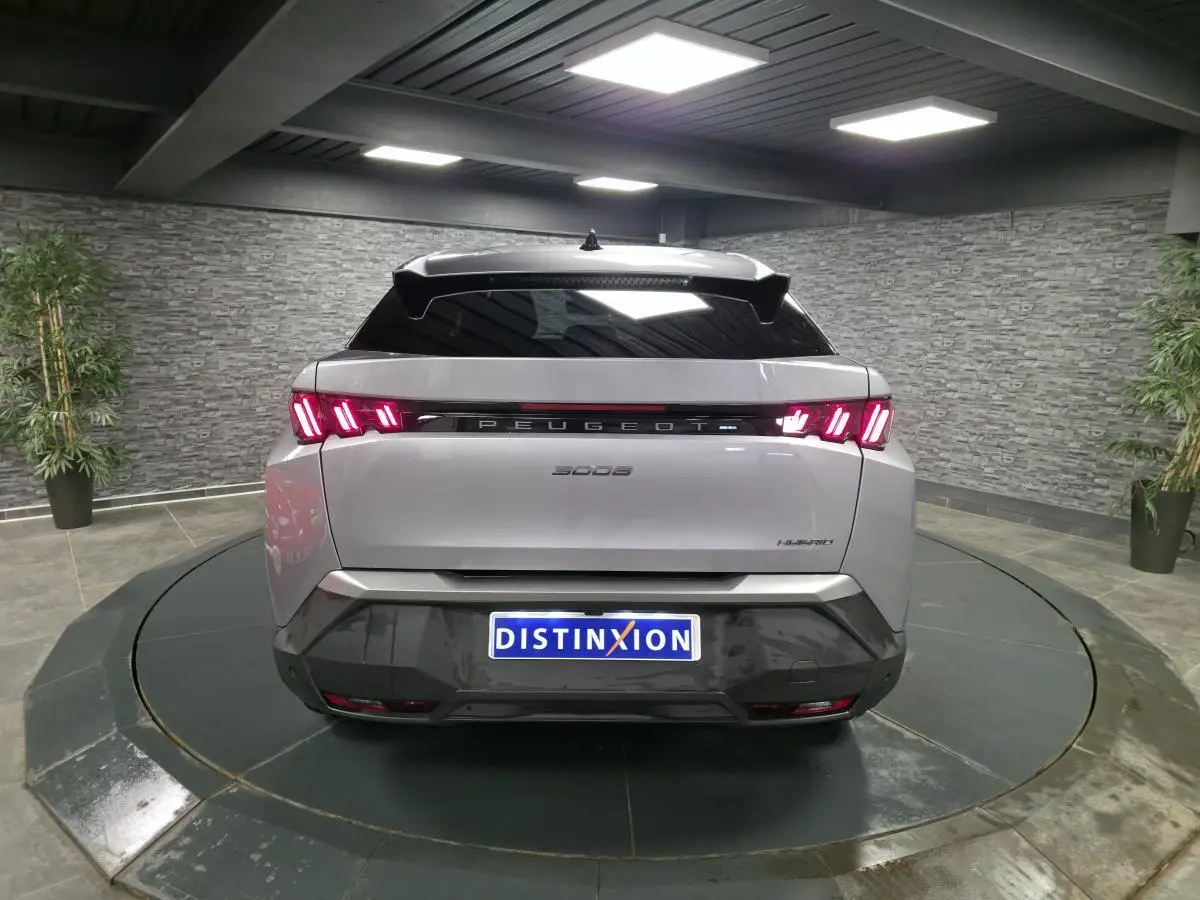 Vue arrière d'un Peugeot 3008 gris métallisé avec feux LED 3 griffes et bandeau noir laqué entre les feux dans un showroom.