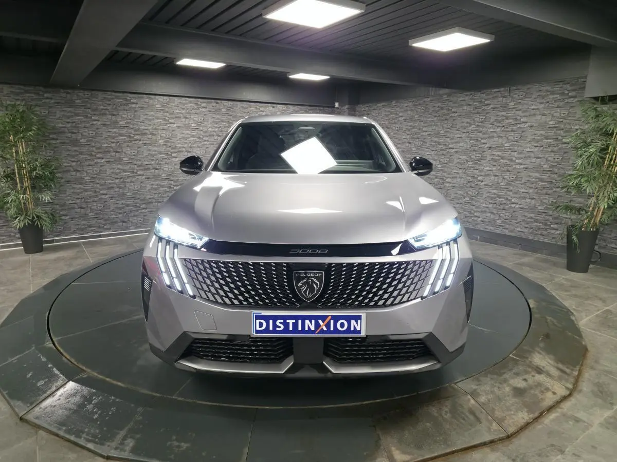Vue avant frontale d'un Peugeot 3008 gris métallisé avec calandre noire laquée et feux LED allumés dans un showroom.