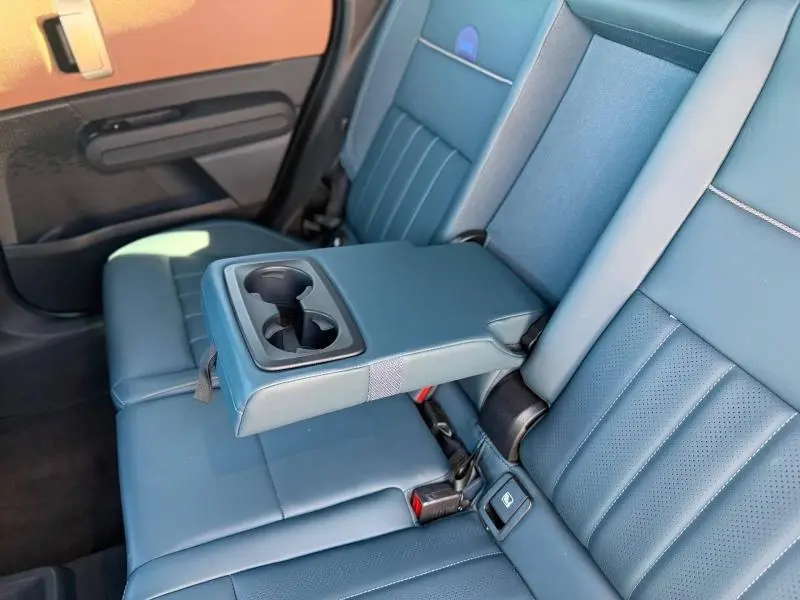 Vue intérieure des sièges arrière bleu foncé du MINI Countryman 2024 avec accoudoir central et porte-gobelets déployé.