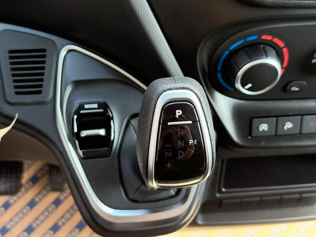 Gros plan sur le levier de vitesses automatique noir et argenté du tableau de bord du Iveco Daily blanc, avec commande mode visible.