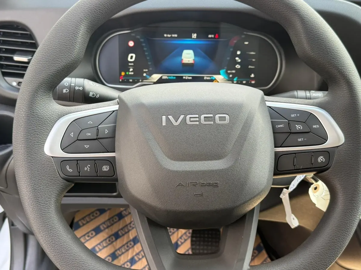 Vue rapprochée du volant gris foncé de l'Iveco Daily 2026 avec commandes intégrées et tableau de bord numérique en arrière-plan.