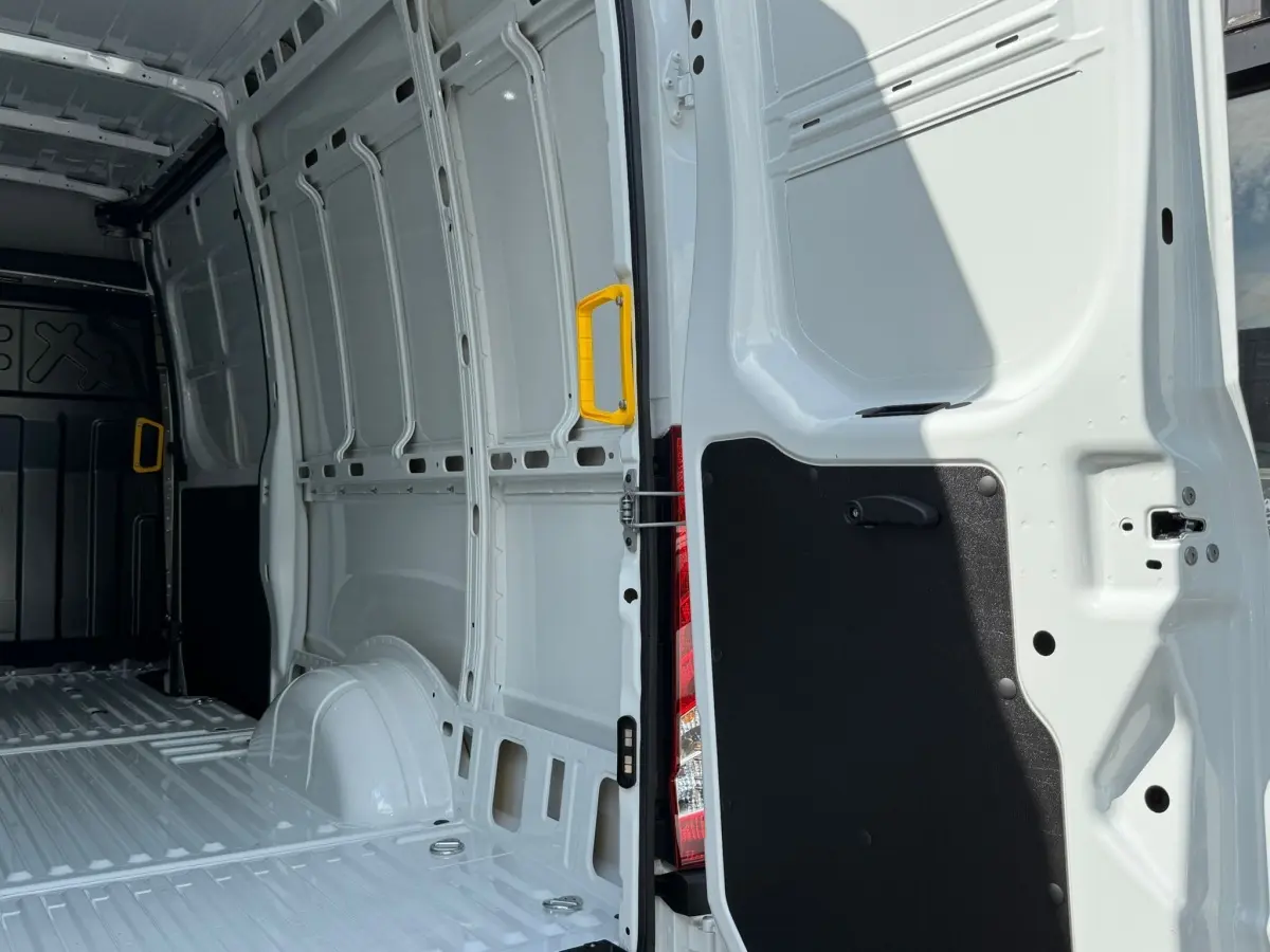 Vue intérieure arrière du fourgon Iveco Daily blanc 2026, montrant la porte ouverte avec poignée jaune et espace de chargement vide.