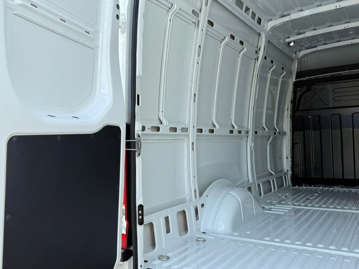 Vue intérieure arrière du fourgon Iveco Daily blanc, montrant l'espace de chargement vide et les parois métalliques.