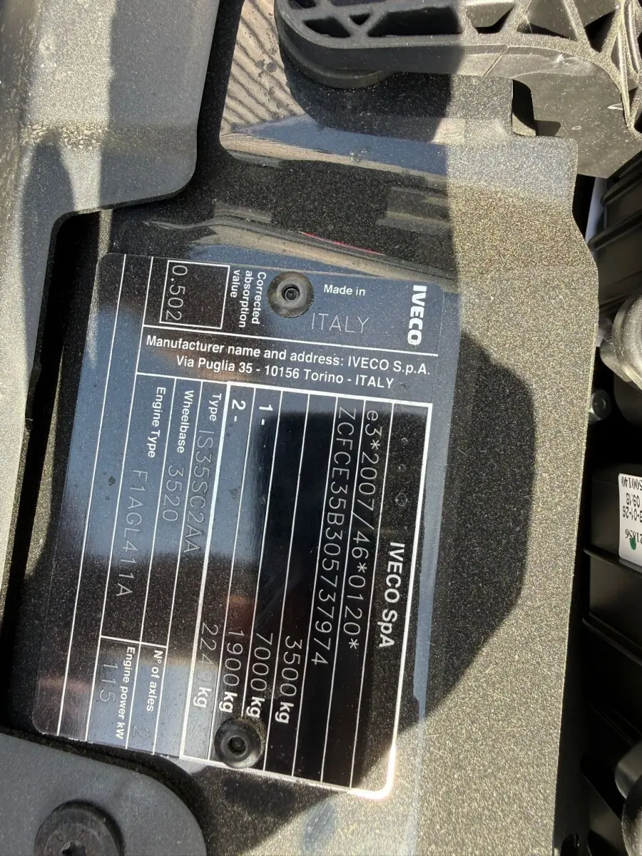 Gros plan sur la plaque constructeur noire du moteur d’un Iveco Daily blanc, montrant les détails techniques et l’origine Italie.