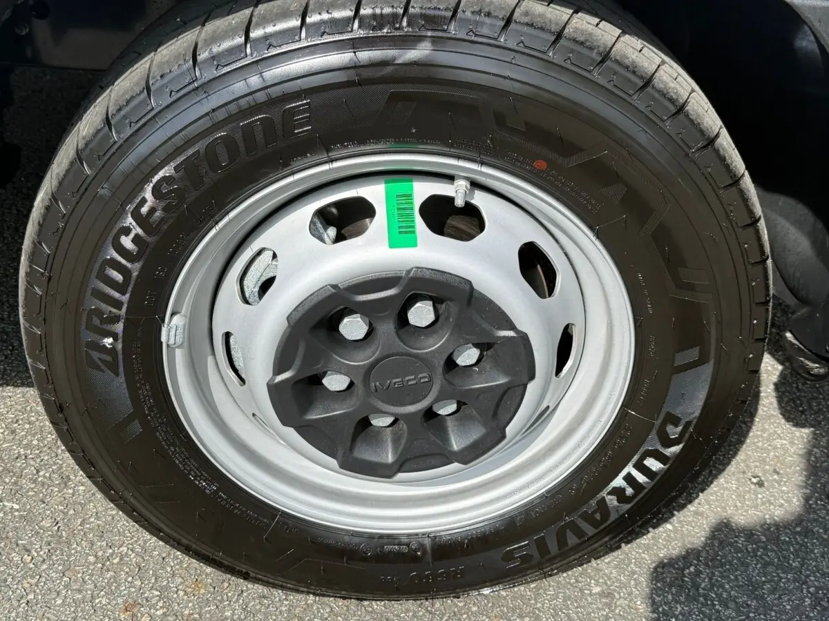 Gros plan sur la roue avant droite d’un Iveco Daily blanc, pneu Bridgestone et jante acier grise avec cache central noir.