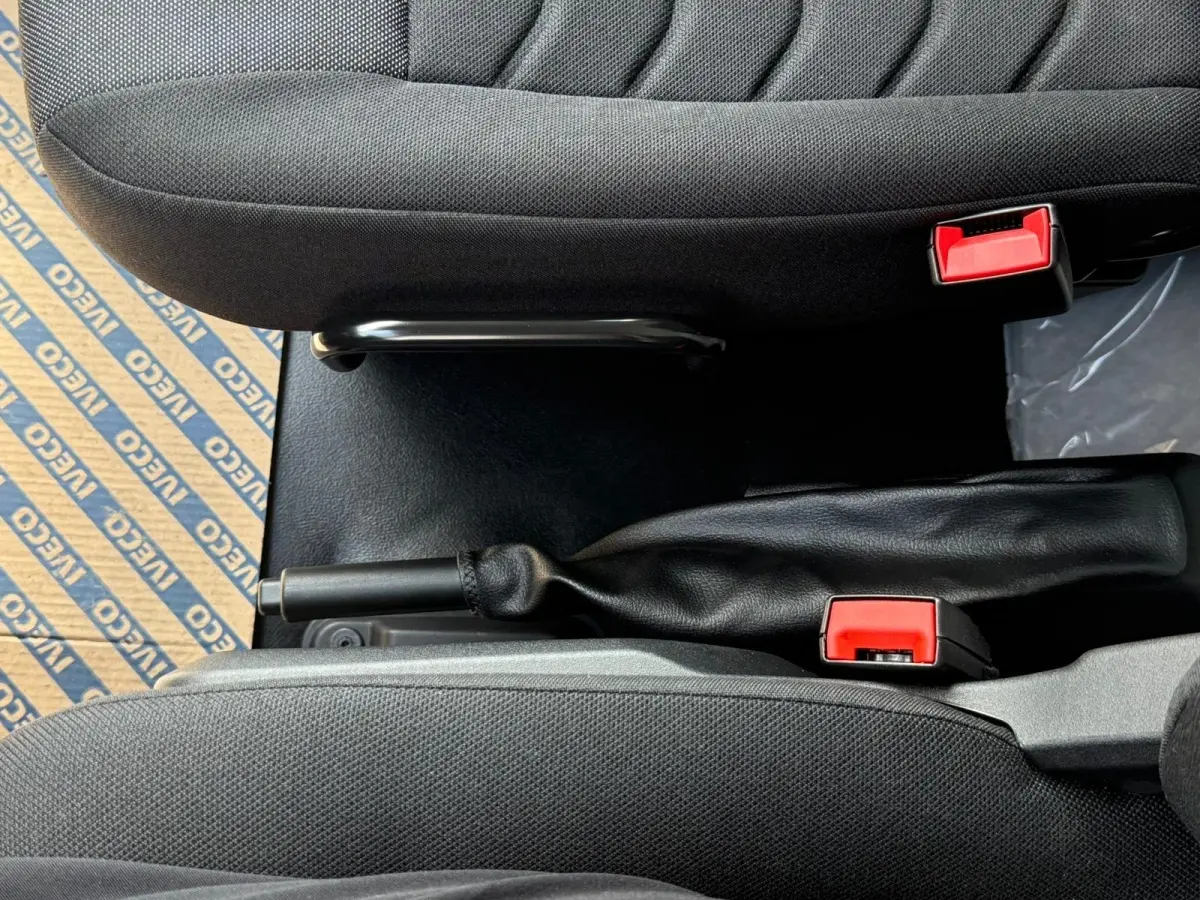Vue rapprochée de la console centrale intérieure du Daily IVECO blanc, montrant le frein à main et les ceintures de sécurité rouges.