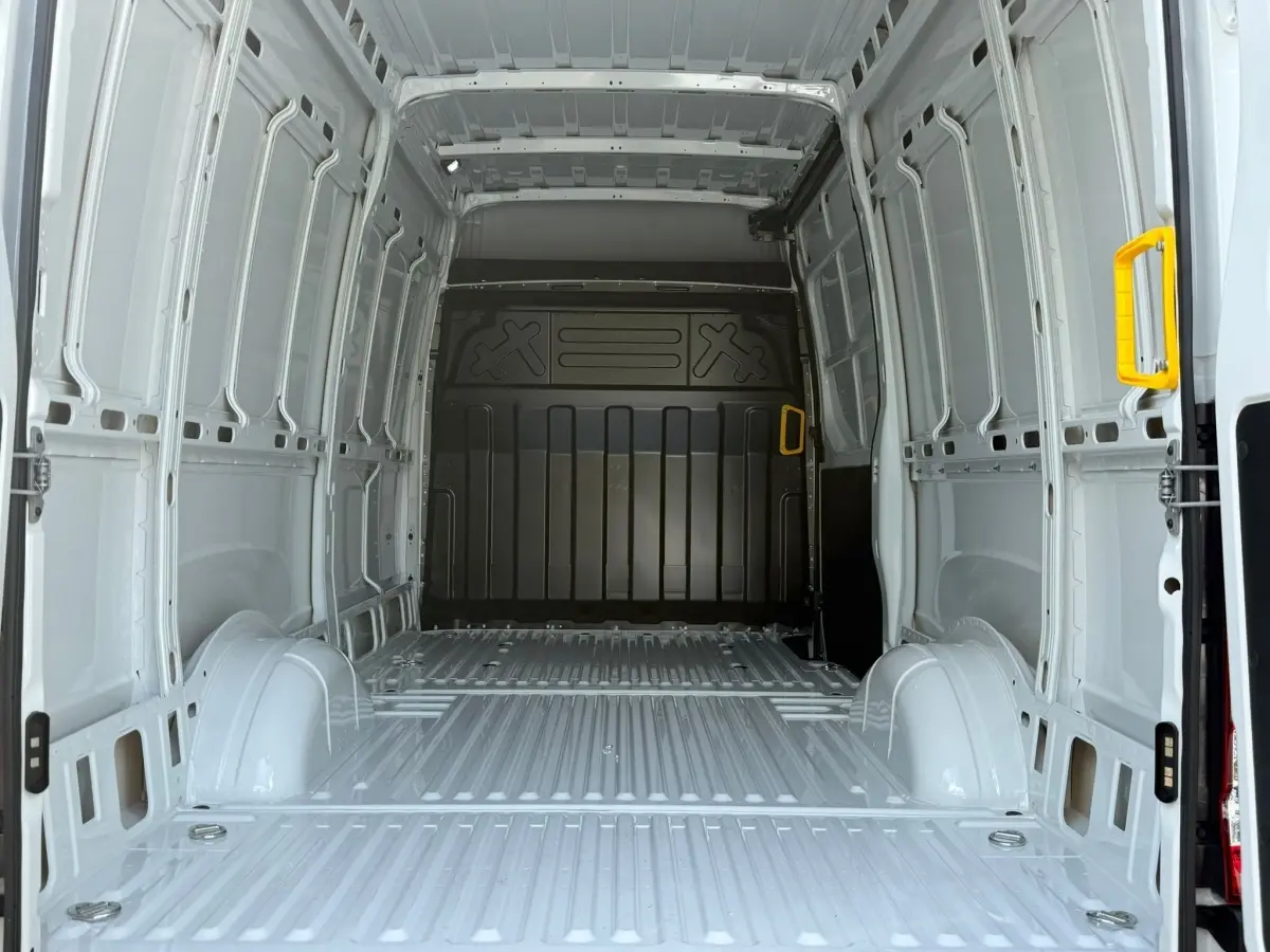 Vue intérieure arrière du fourgon Iveco Daily blanc 2026, montrant la grande zone de chargement vide avec poignées jaunes.