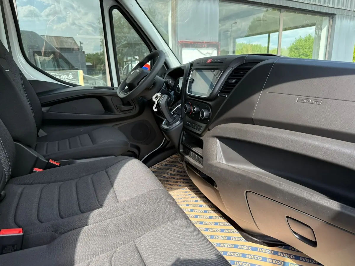 Vue intérieure côté conducteur du fourgon Iveco Daily 2.3 blanc, avec tableau de bord noir et sièges gris foncé.