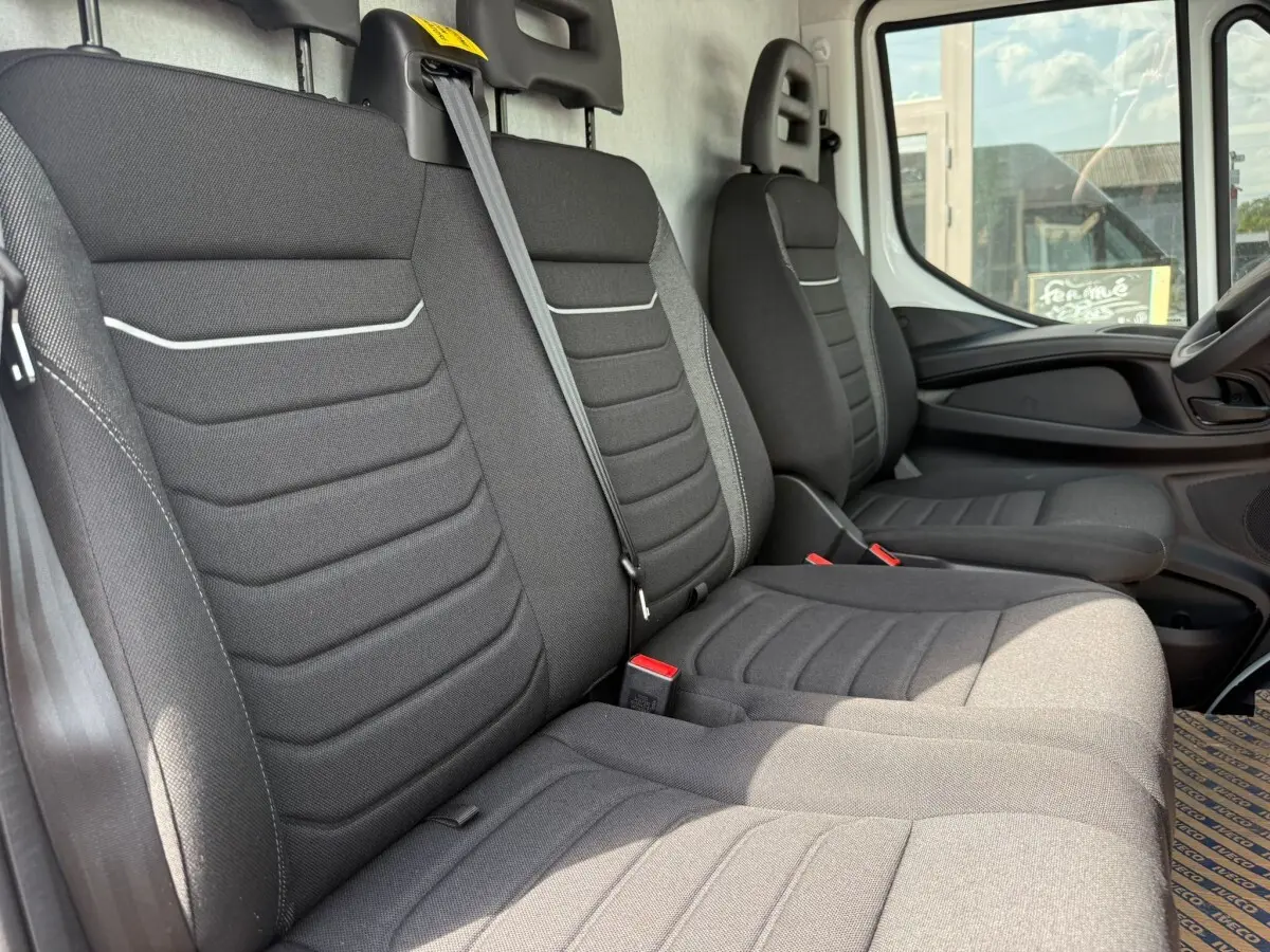 Vue intérieure côté passager montrant les sièges gris foncé du fourgon Iveco Daily 2026 avec ceinture de sécurité visible.