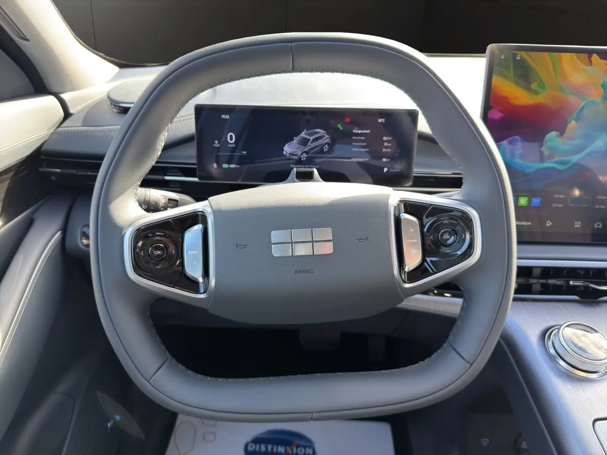 Vue intérieure centrée sur le volant gris clair du Geely E5 2026 avec tableau de bord numérique et écran tactile coloré.
